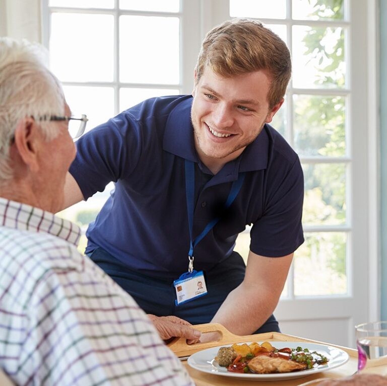 Male,care,worker,serving,dinner,to,a,senior,man,at